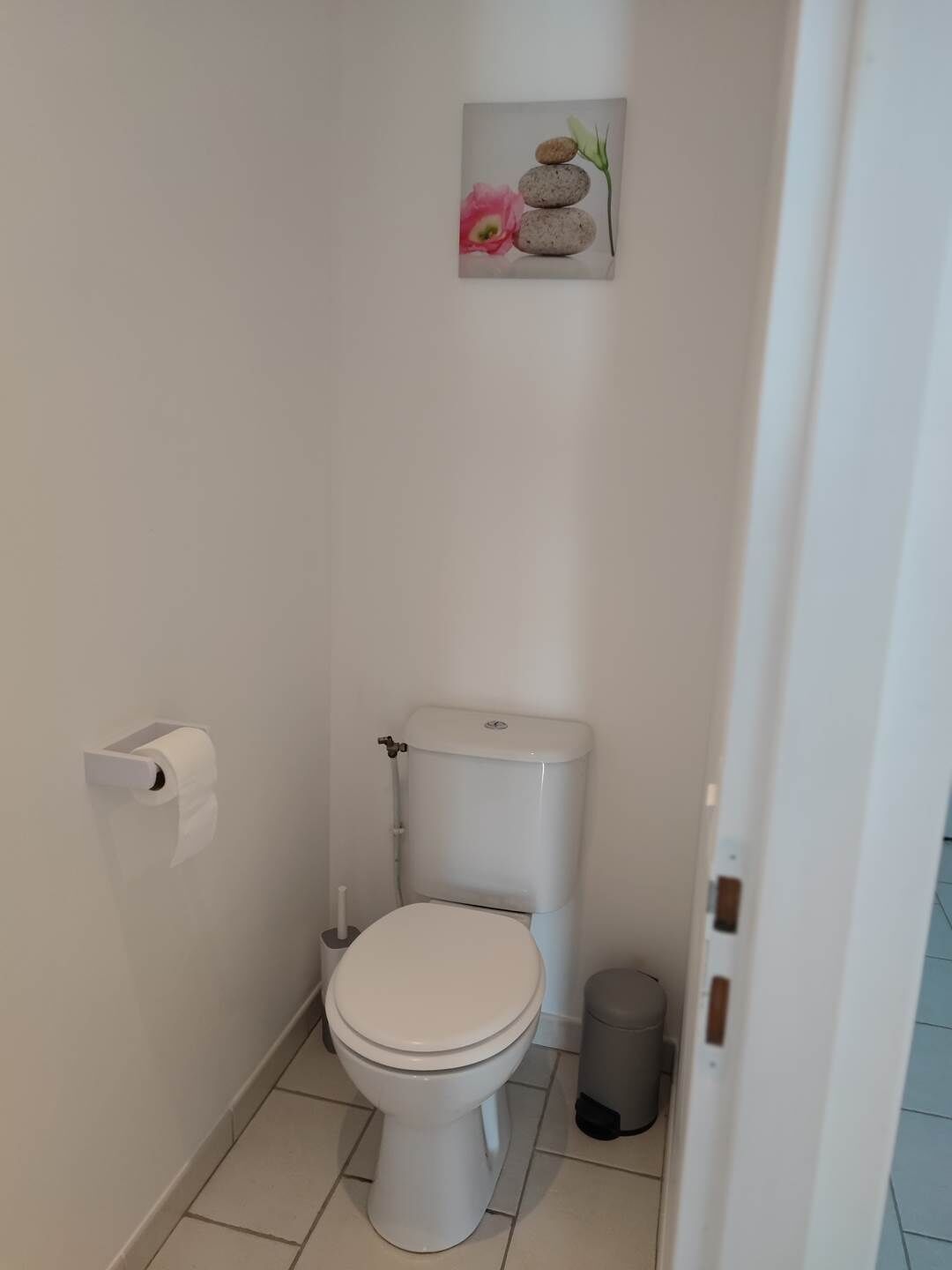 Et lille, rent badeværelse med toilet, skraldespand og toiletpapirholder.