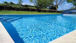 Una piscina azul cristalina con borde de piedra, rodeada de césped y árboles.