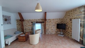 Una sala de estar acogedora con pared de piedra, viga de techo de madera, un sofá, una silla, un televisor y una chimenea.