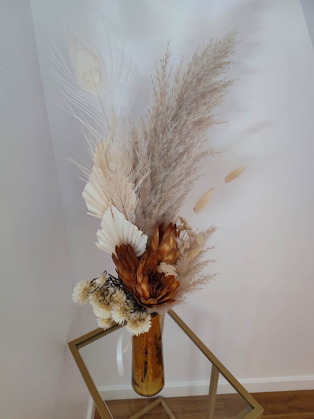 Un florero con flores secas y hierba de pampa sobre un soporte metálico geométrico.