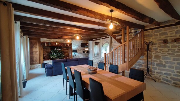 Een gezellig eetgedeelte met een houten tafel en stoelen, een stenen openhaard en een trap naar een hoger gelegen verdieping.