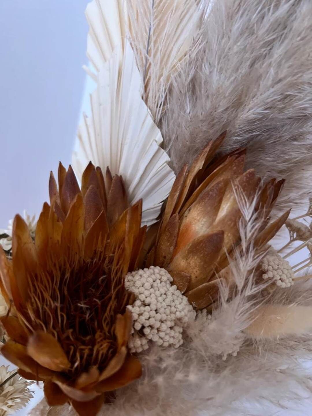 Primer plano de una composición decorativa con una flor marrón grande, plumas blancas y esferas blancas.