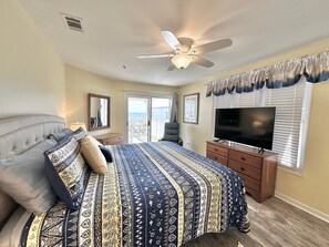 Un dormitorio con una cama grande, un ventilador de techo, un televisor y vistas al exterior.