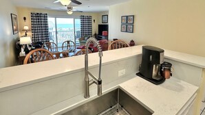 A modern kitchen with a built-in dishwasher, a coffee maker, and a dining area with a table and chairs. - Summer & July 4th Savings at Beachside Colony Tybee's ONLY Oceanfront Resort 3/2 (Tybee Island)