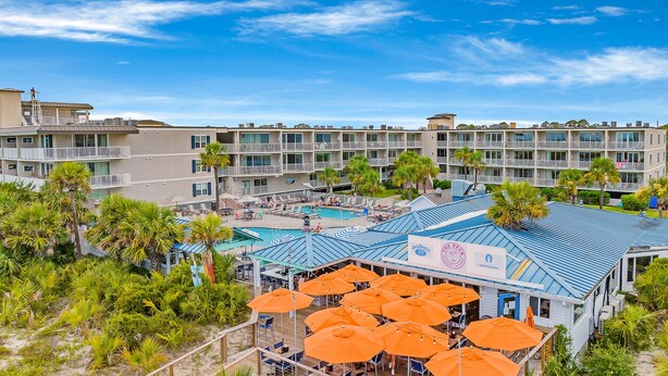 A resort with a pool area, outdoor seating with umbrellas, and a view of the surrounding buildings. - Summer & July 4th Savings at Beachside Colony Tybee's ONLY Oceanfront Resort 3/2 (Tybee Island)