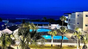 A pool area with palm trees, a building with balconies, and a view of the ocean. - Summer & July 4th Savings at Beachside Colony Tybee's ONLY Oceanfront Resort 3/2 (Tybee Island)