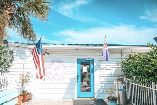 A white building with a blue door, two flags, and a logo reading "The Deck Beachfront Kitchen".