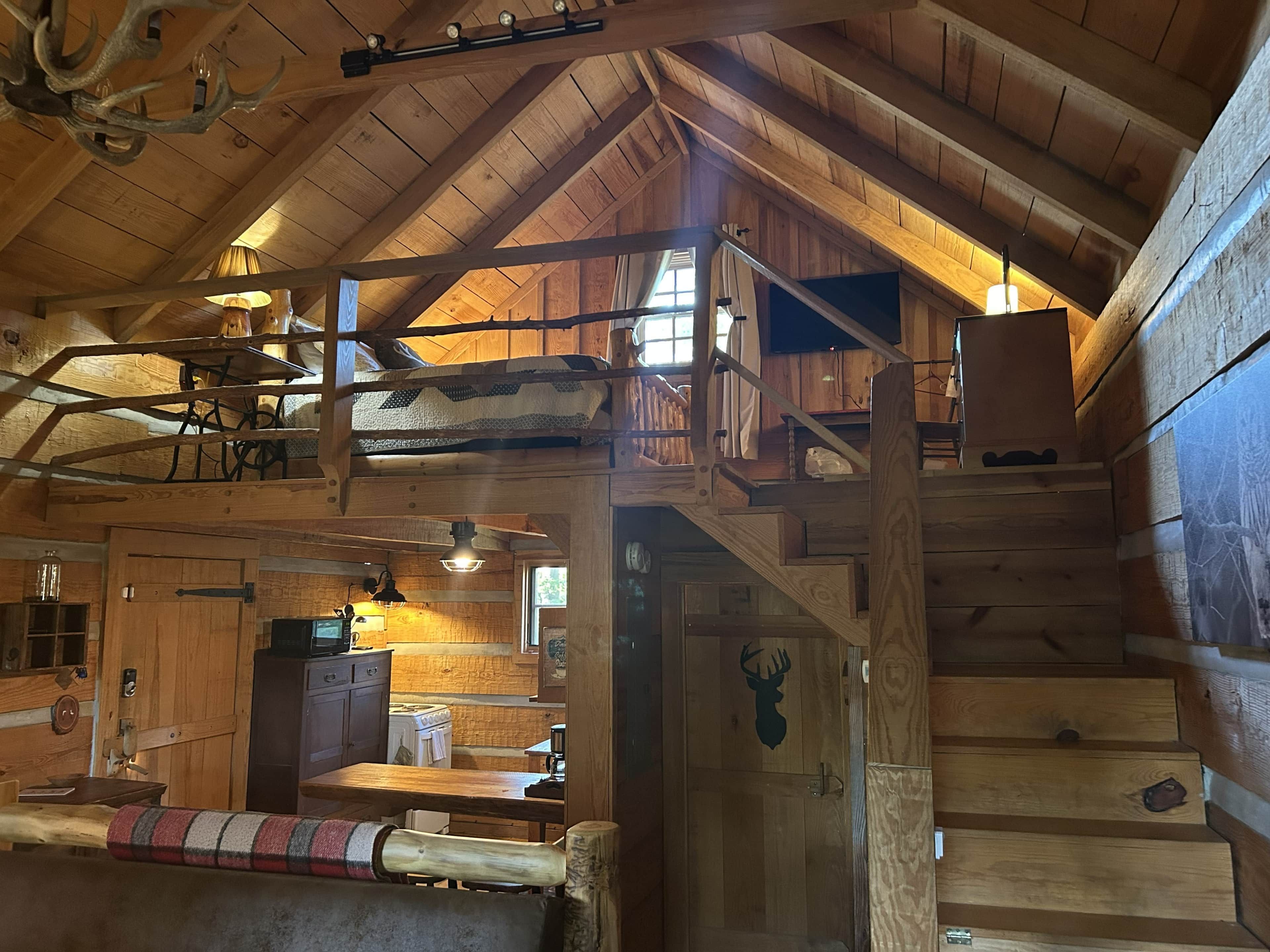 Un interno rustico con camera da letto in soppalco, scala in legno e angolo cottura.