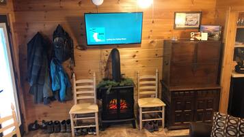 Een gezellig chaletinterieur met een open haard, twee stoelen, een aan de muur bevestigde televisie en een houten kast.