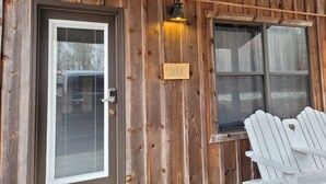 Facciata in legno con una porta, una finestra e un cartello con un numero.