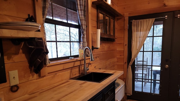 Una cucina in legno con un lavello, una finestra con tende e una porta che dà all'esterno.