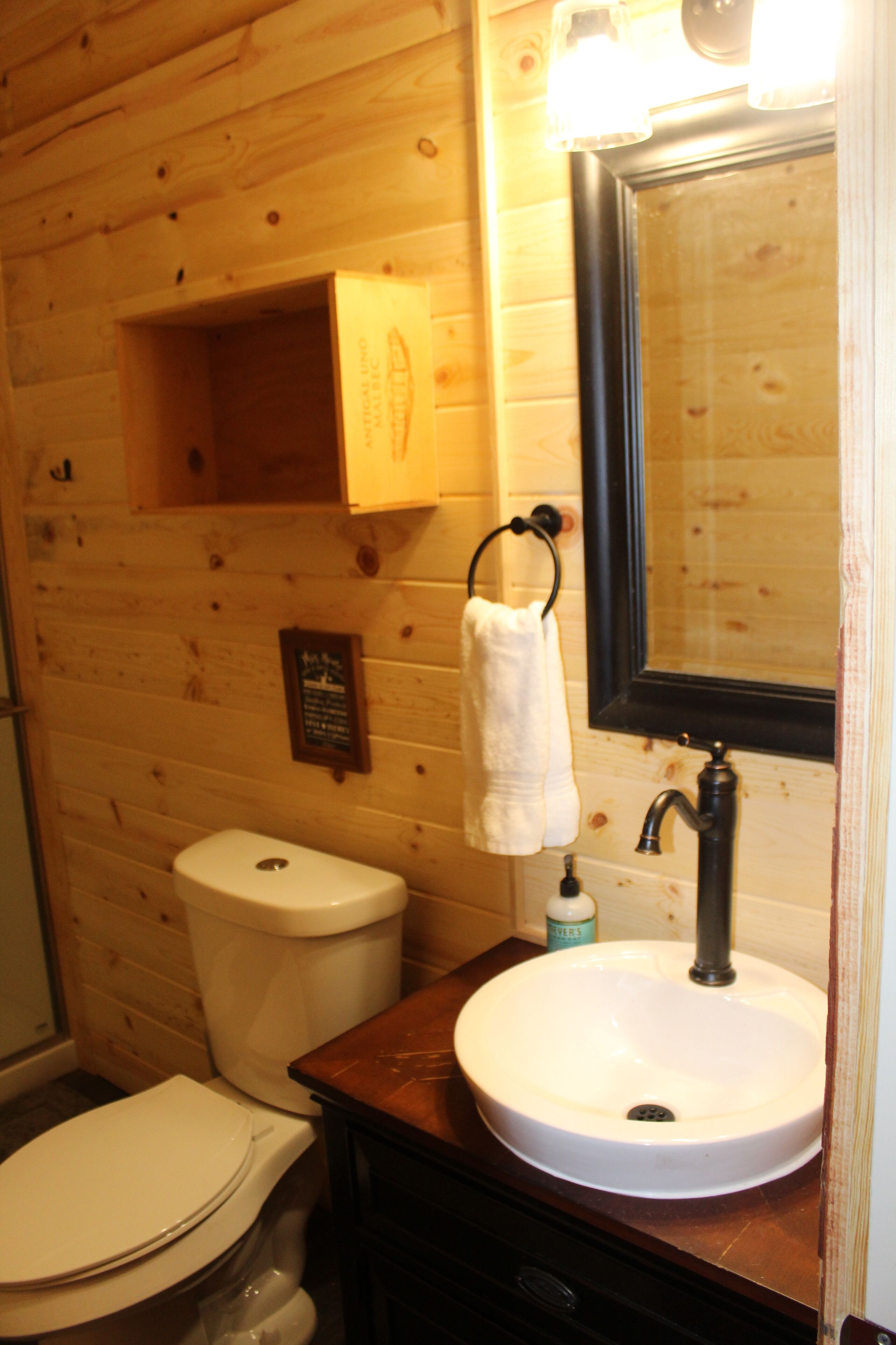 A wooden cabin bathroom with a toilet, sink, and mirror.