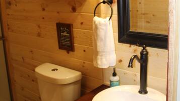 A wooden cabin bathroom with a toilet, sink, and mirror.