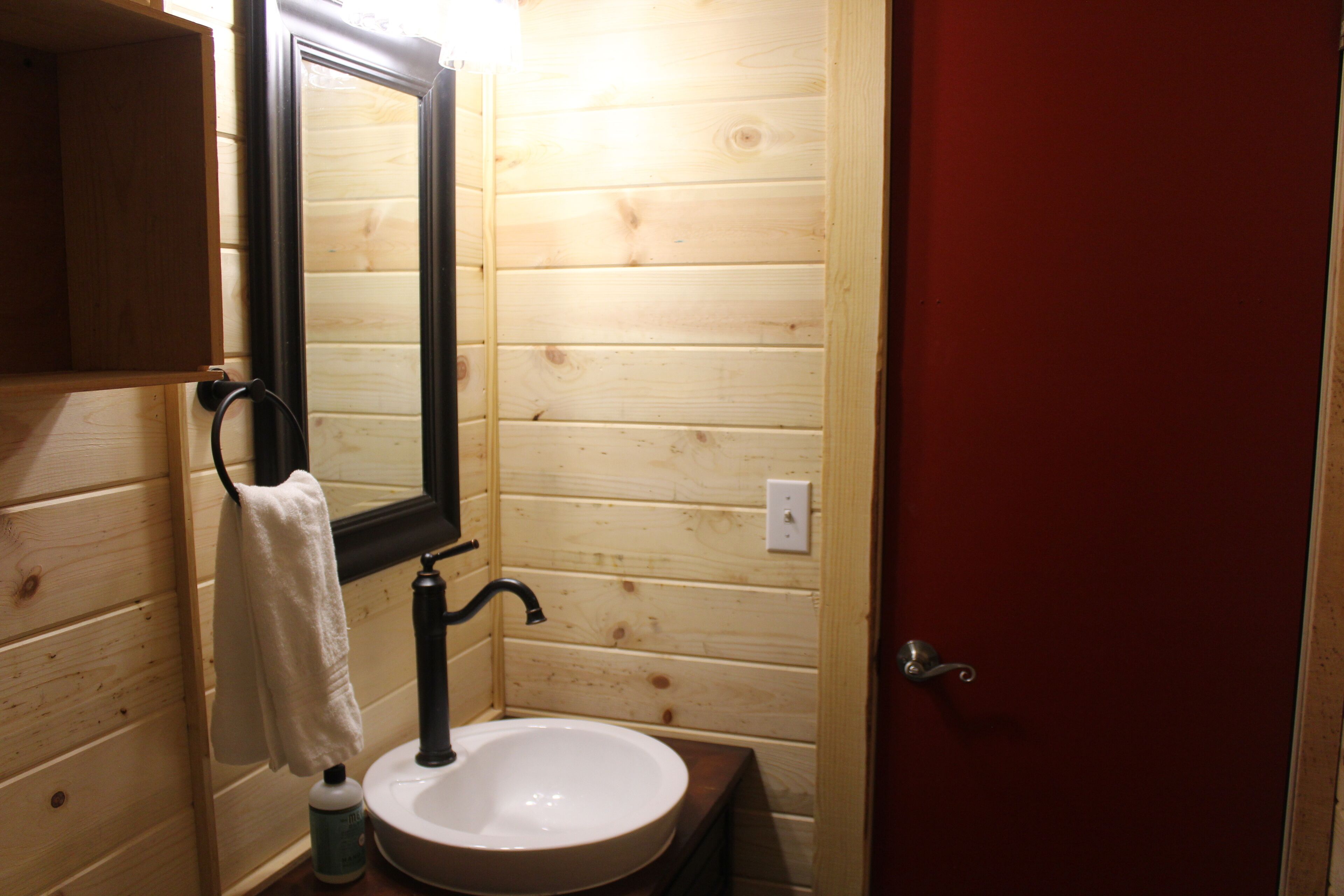 A wooden cabin bathroom with a sink, mirror, and towel hanging on the wall.