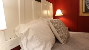 A bed with white bedding and a patterned pillow in a room with red walls and a white door. - Millers Landing 1 - Sleeps 6. MINUTES to Lower Buffalo River (Yellville)