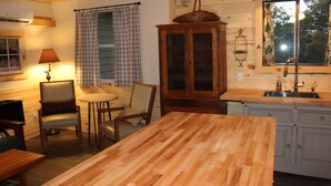 A wooden dining table with chairs, a cabinet, a window with curtains, and a sink in a cabin-style kitchen. - Millers Landing 1 - Sleeps 6. MINUTES to Lower Buffalo River (Yellville)
