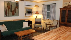 A cozy living room with a green sofa, wooden coffee table, and a dining table. There is a ceiling fan, a lamp, and a window with a view of the outdoors. - Millers Landing 1 - Sleeps 6. MINUTES to Lower Buffalo River (Yellville)