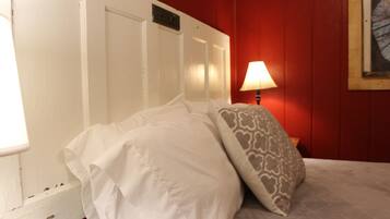 A bed with white bedding and a patterned pillow in a room with red walls and a white door.