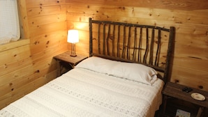 Een slaapkamer in chaletstijl met een bed, een nachtkastje, een lamp en een raam met gordijn.