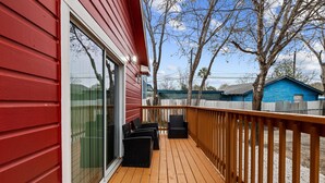 A wooden deck with outdoor furniture, a glass door, and a view of a blue house and trees. - Inviting 4br/2.5ba Downtown Home With Ample Space! (San Antonio)