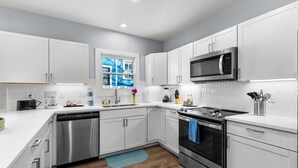 A modern kitchen with white cabinets, stainless steel appliances, and a window with a cityscape view. - Inviting 4br/2.5ba Downtown Home With Ample Space! (San Antonio)