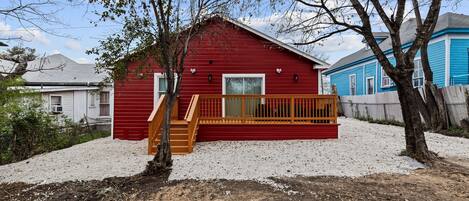 A red wooden cabin with a wooden deck and a small staircase leading to a door.