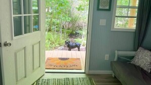A room with a door leading to a garden, a small wooden bench, and a framed picture on the wall.