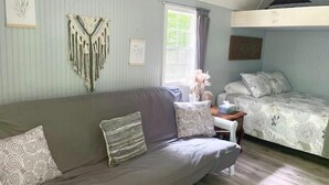 A cozy room with a grey sofa, a small table with a vase, and a bunk bed with patterned bedding.