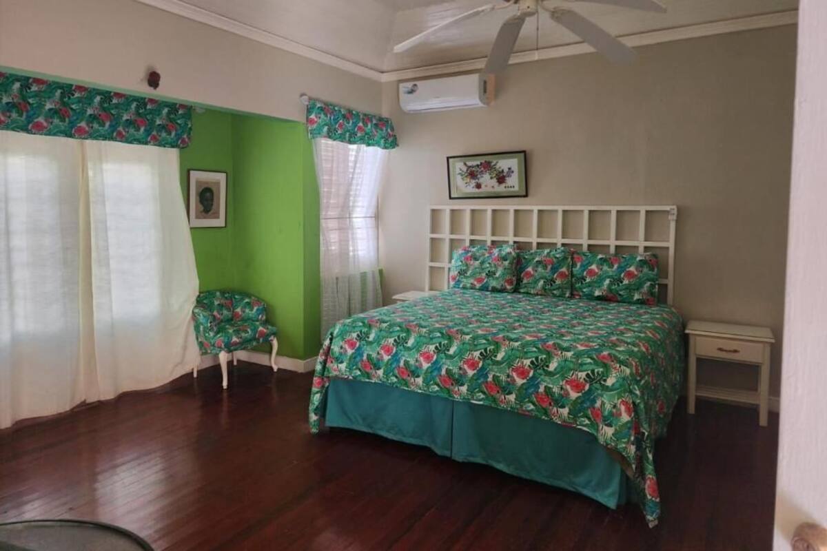 A bedroom with a bed, a chair, a ceiling fan, and a window with curtains.