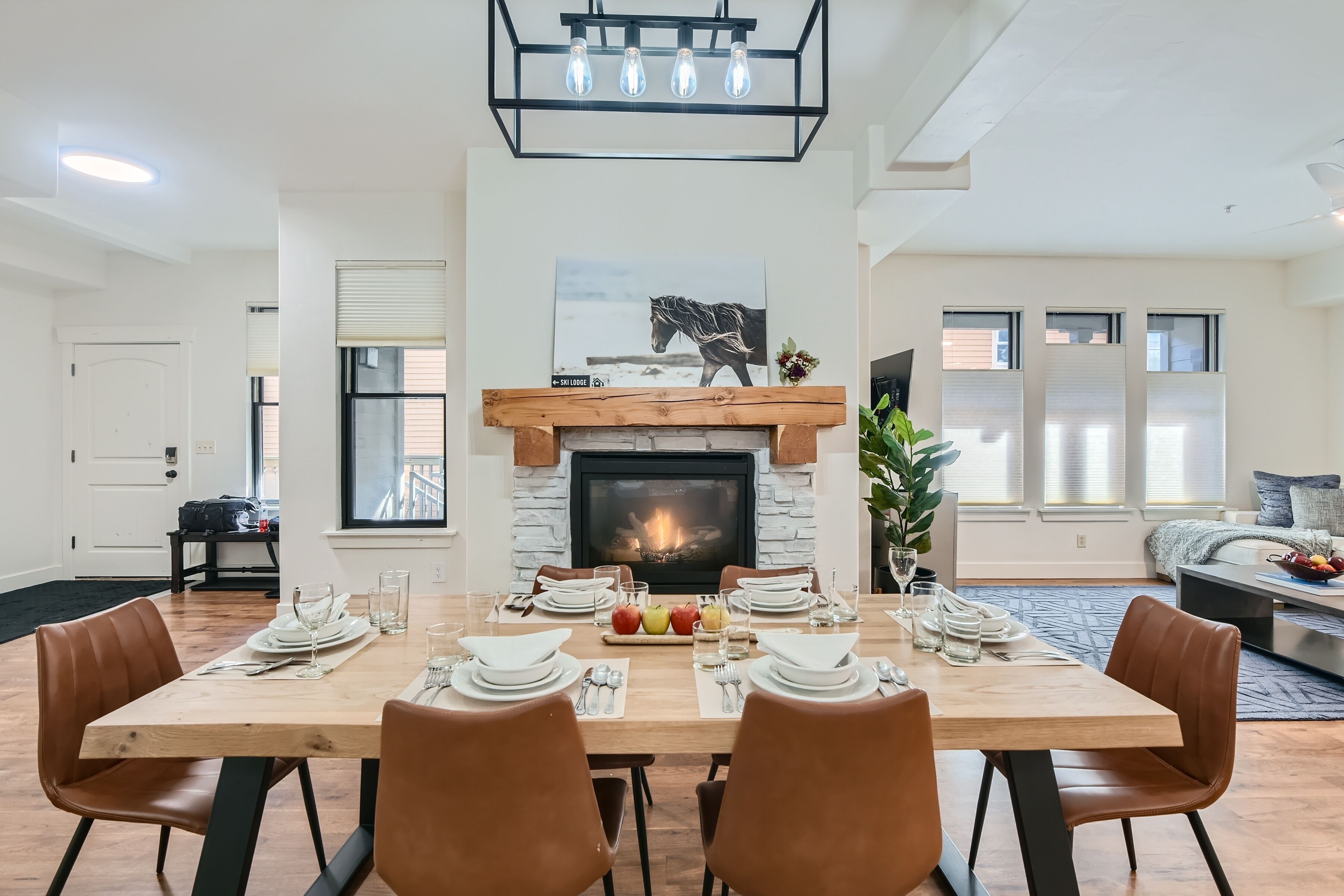A dining area with a fireplace, a dining table set for four, and a living room in the background.