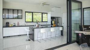A modern kitchen with a large island, bar stools, and a built-in grill. - Luxurious 6-Bedroom Villa with Private Pier & Panoramic Ocean View (Jeremi)