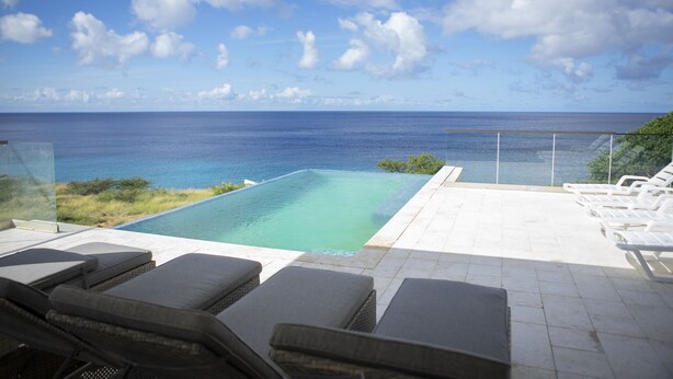 A pool with a view of the ocean, lounge chairs, and a glass barrier. - Luxurious 6-Bedroom Villa with Private Pier & Panoramic Ocean View (Jeremi)