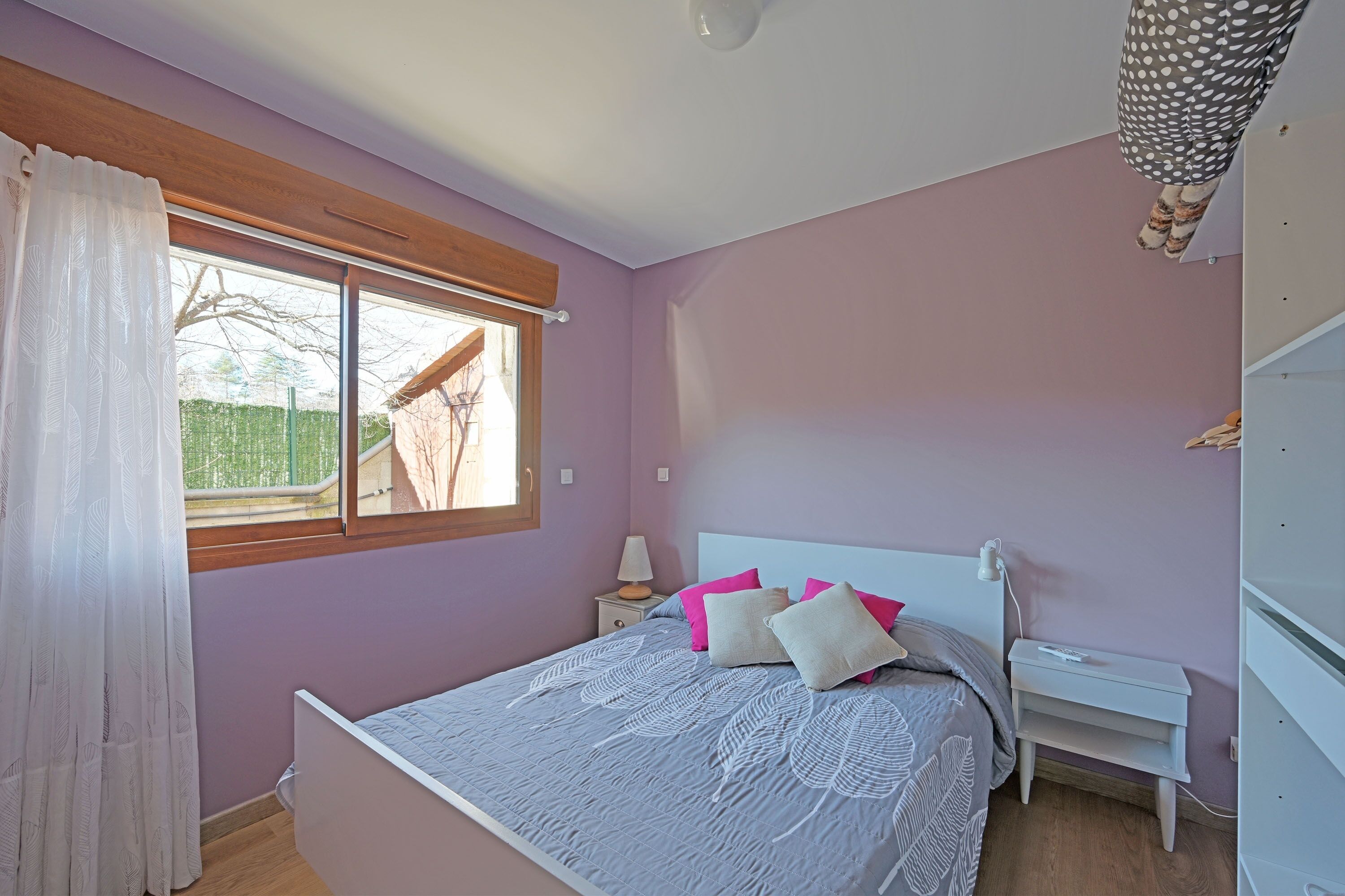 Een slaapkamer met een bed, nachtkastjes, een lamp en een raam met gordijnen.