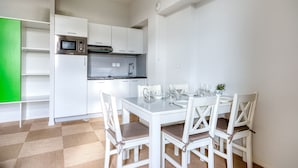 A modern kitchen with white cabinets, a microwave, and a stainless steel refrigerator. There is a dining table with white chairs and a green wall in the background. - Kergonano - Parking privé et piscine (Baden)