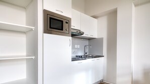 A compact kitchen with white cabinets, a stainless steel microwave, and a built-in oven. - Kergonano - Parking privé et piscine (Baden)