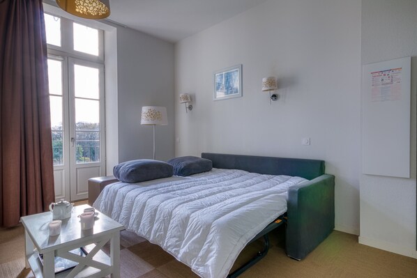 Une chambre à coucher avec un lit, une table sur laquelle se trouvent des tasses et une théière, une fenêtre avec des rideaux et des lampes fixées au mur.