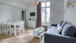 A modern living room with a dining area, a sofa, a coffee table, and a TV mounted on the wall. - Kergonano - Parking privé et piscine (Baden)