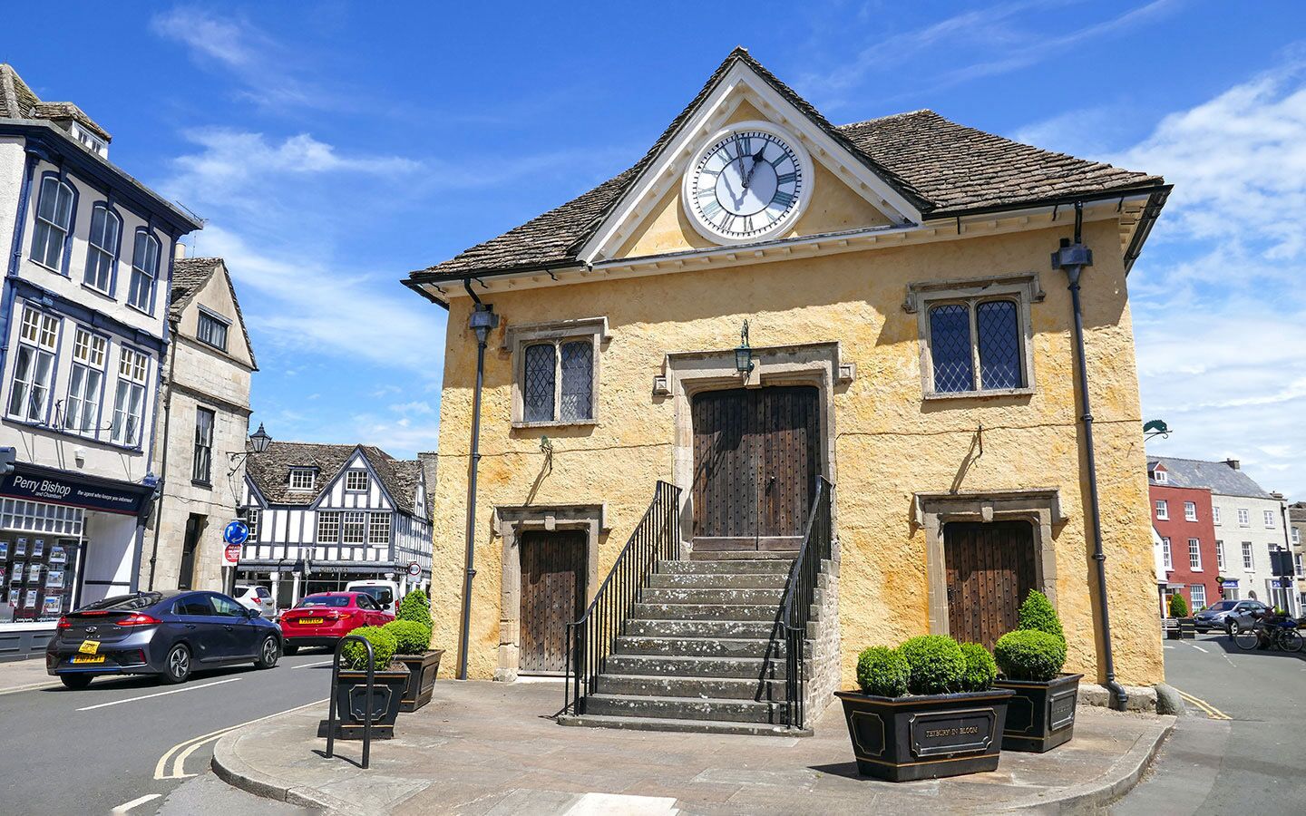 A two-story building with a clock on the front, a staircase leading to the entrance, and a street in front.