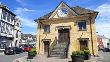 A two-story building with a clock on the front, a staircase leading to the entrance, and a street in front.