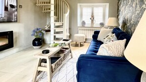 A living room with a blue sofa, a white spiral staircase, a fireplace, and a window with blinds.