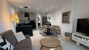 Een moderne woonkamer met een bank, twee salontafels, een televisie en een eethoek met stoelen en een tafel.