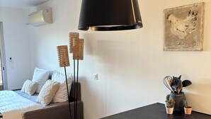 Een moderne slaapkamer met een bed, nachtkastje en een zwart bureau met lades. Er hangt een lamp, is een wandairconditioner en een schilderij van een kip.