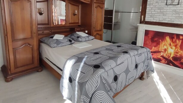 A bedroom with a large bed, wooden headboard, a chandelier, a white brick wall, and a fireplace.