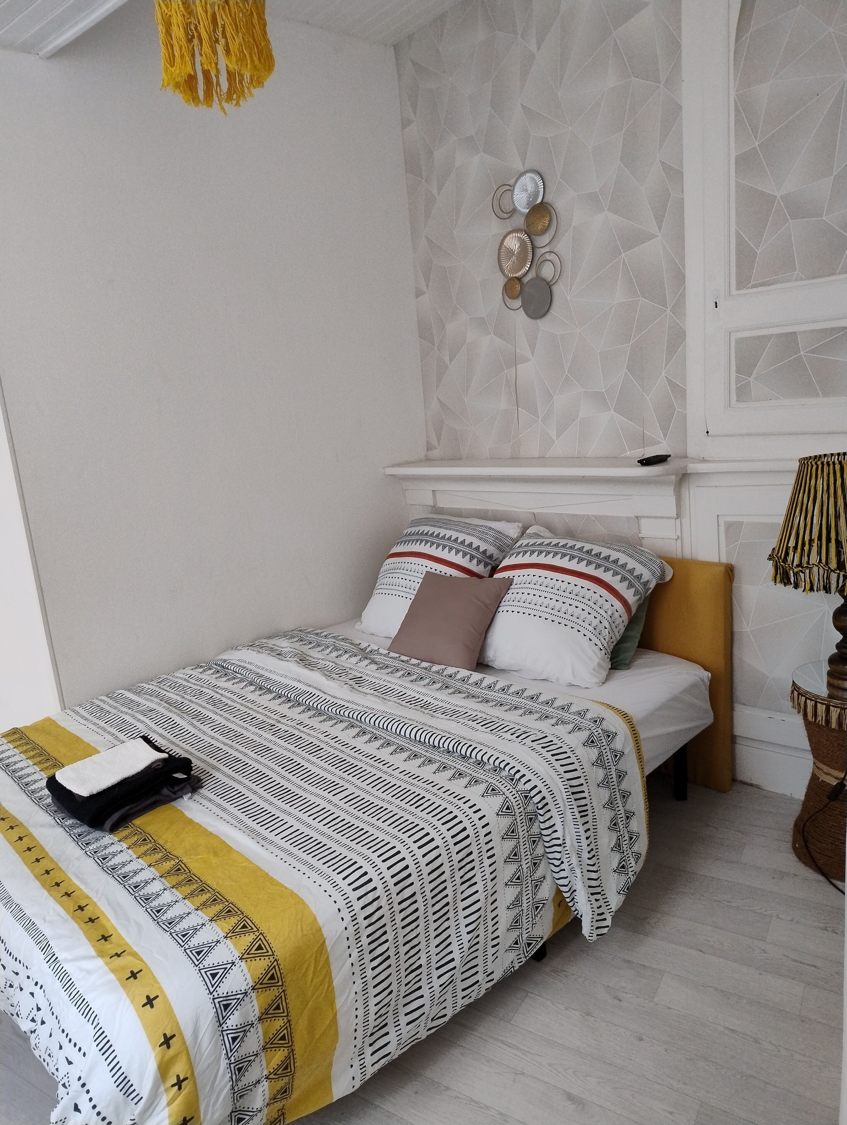 A neatly made bed with patterned bedding, a bedside table with a lamp, and a geometric-patterned wall.