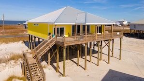 A yellow building with a wooden deck and stairs, located on a sandy beach.