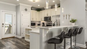 A modern kitchen with white cabinets, a central island with bar stools, stainless steel appliances, and pendant lighting.