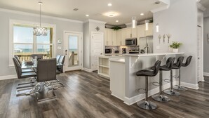 A modern kitchen with a central island, bar stools, and a dining area with a glass table and chairs.