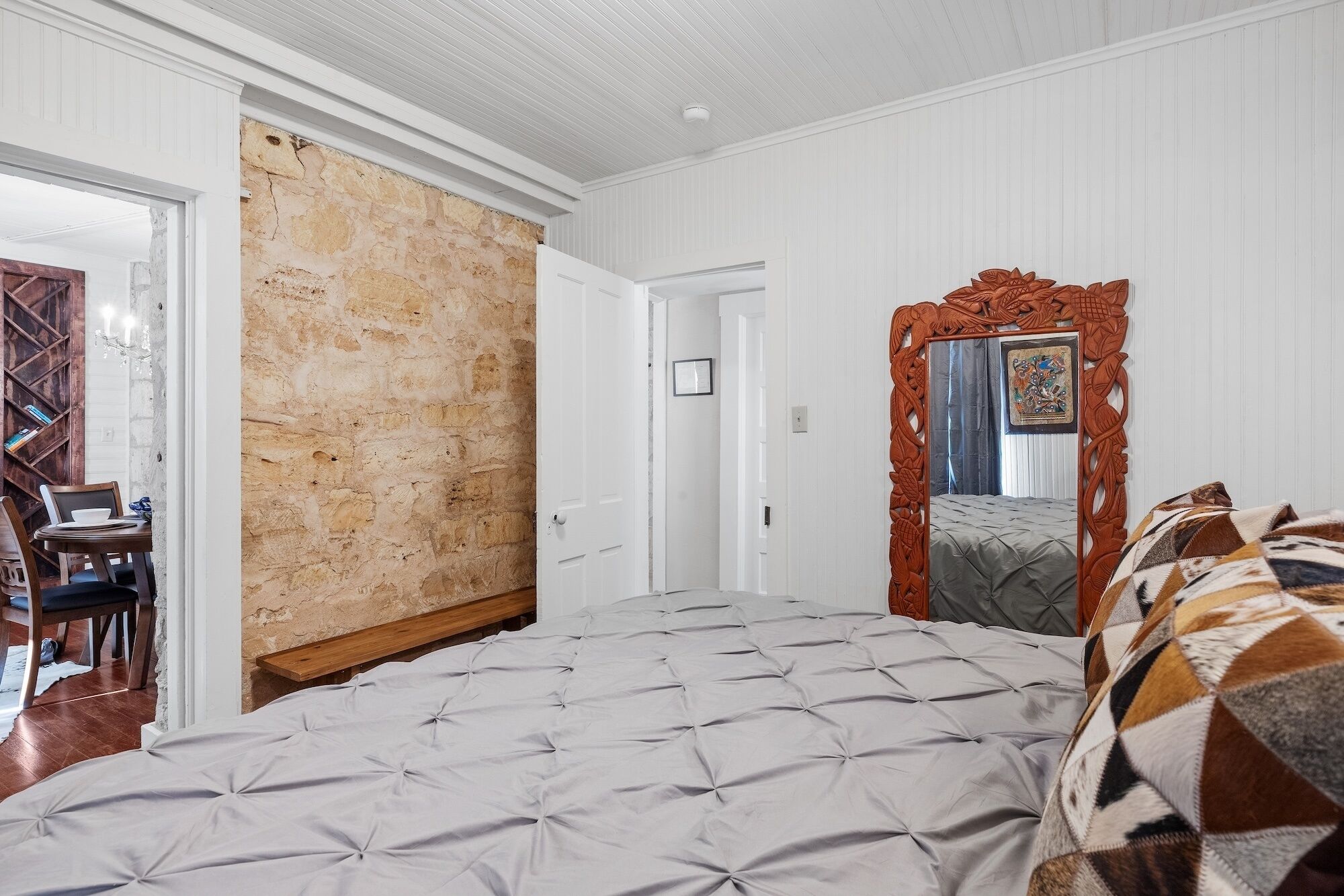 Une chambre à coucher avec un grand lit, un mur en pierre, une porte en bois et un miroir doté d’un cadre orné.