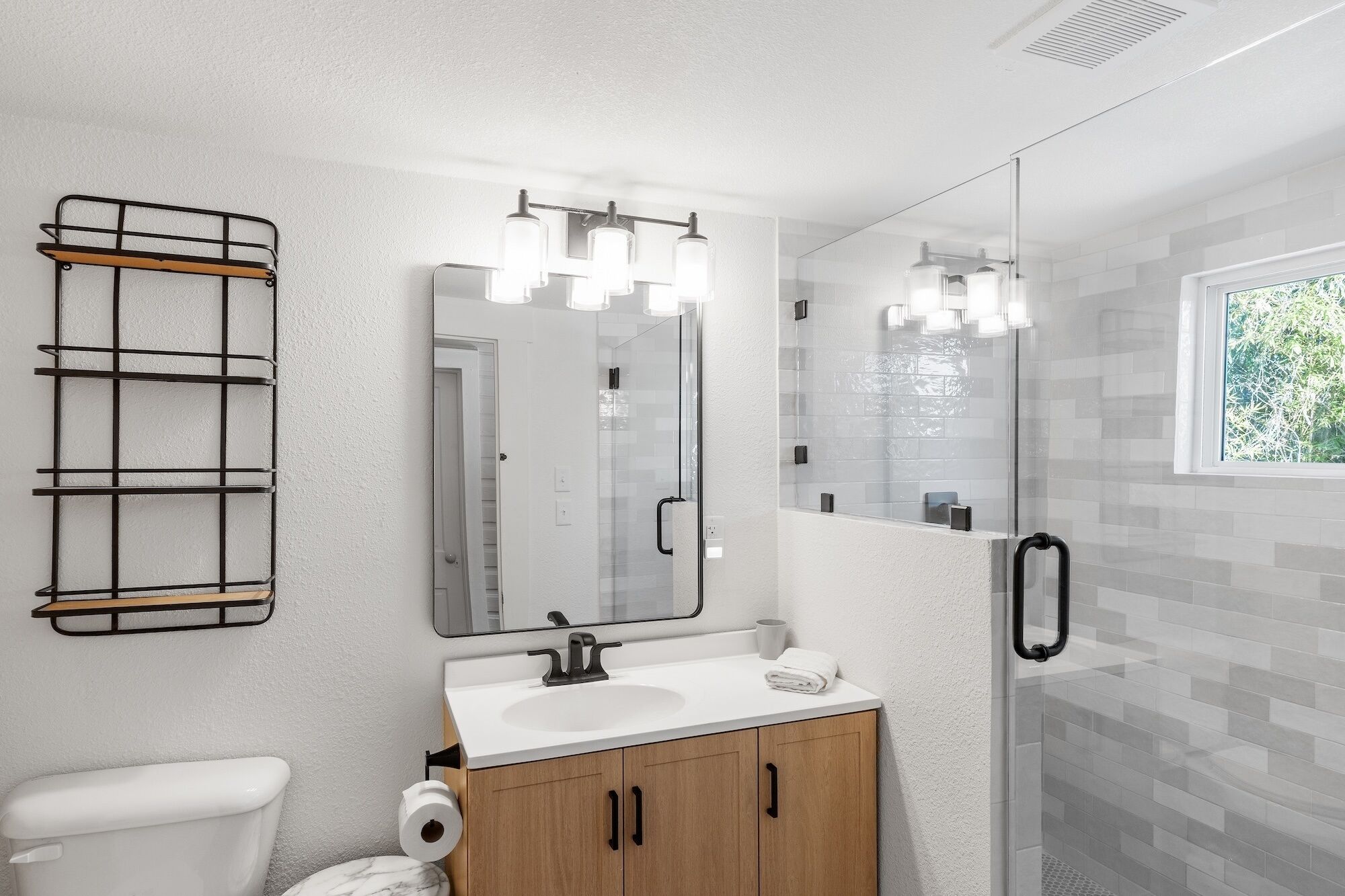 A modern bathroom with a white sink, wooden cabinets, a glass shower enclosure, and a metal towel rack.