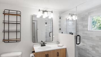 A modern bathroom with a white sink, wooden cabinets, a glass shower enclosure, and a metal towel rack.